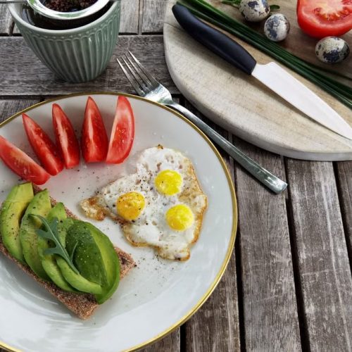 Breakfast setup with avocado toast, quail eggs, and fresh tomatoes on a rustic wooden table.