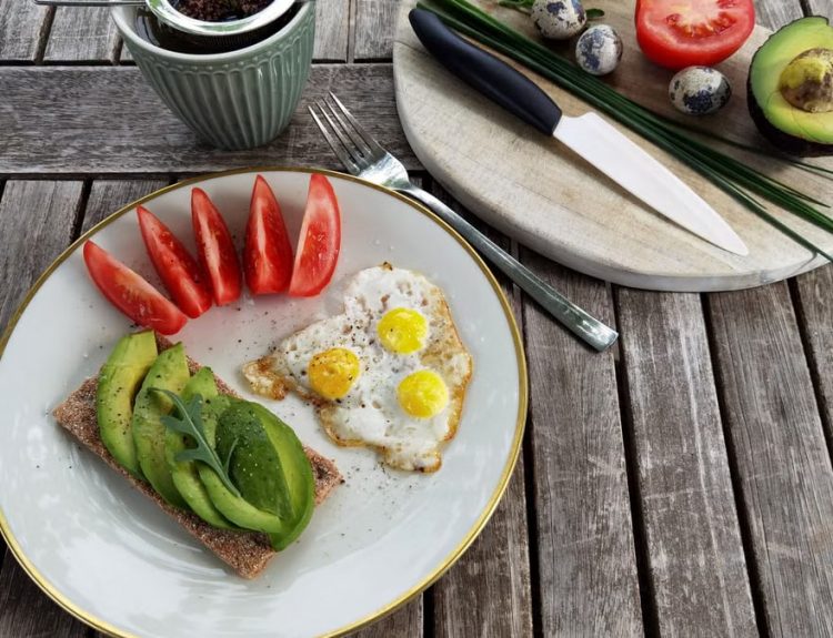 Breakfast setup with avocado toast, quail eggs, and fresh tomatoes on a rustic wooden table.
