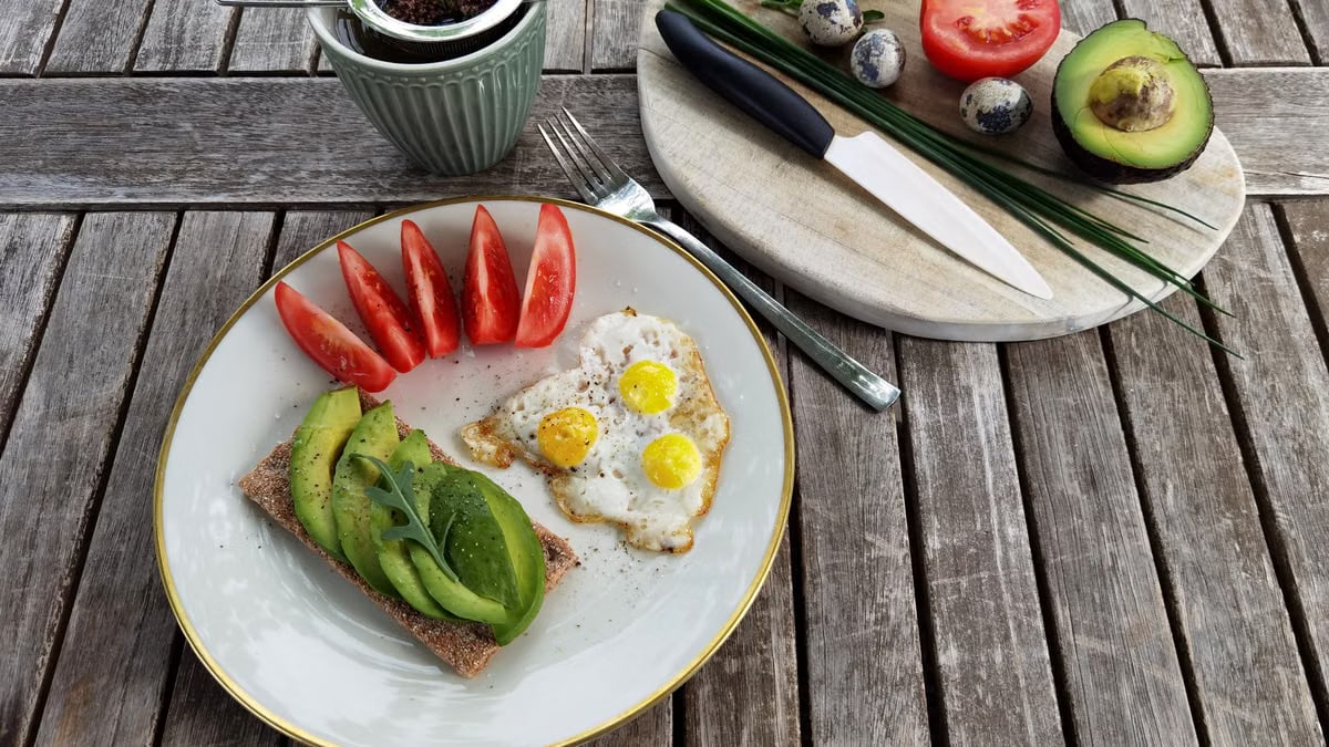 Breakfast setup with avocado toast, quail eggs, and fresh tomatoes on a rustic wooden table.