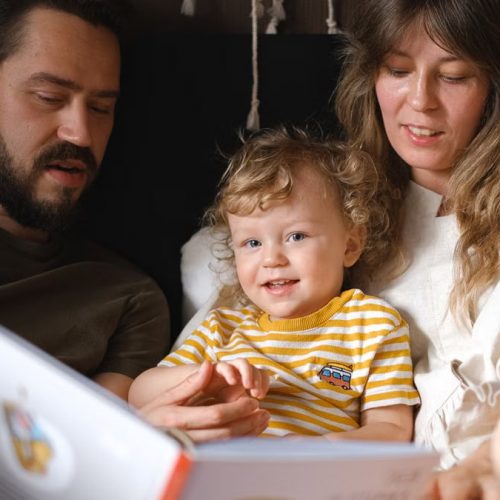 A happy family reading together, featuring parents and their smiling child enjoying a book indoors.